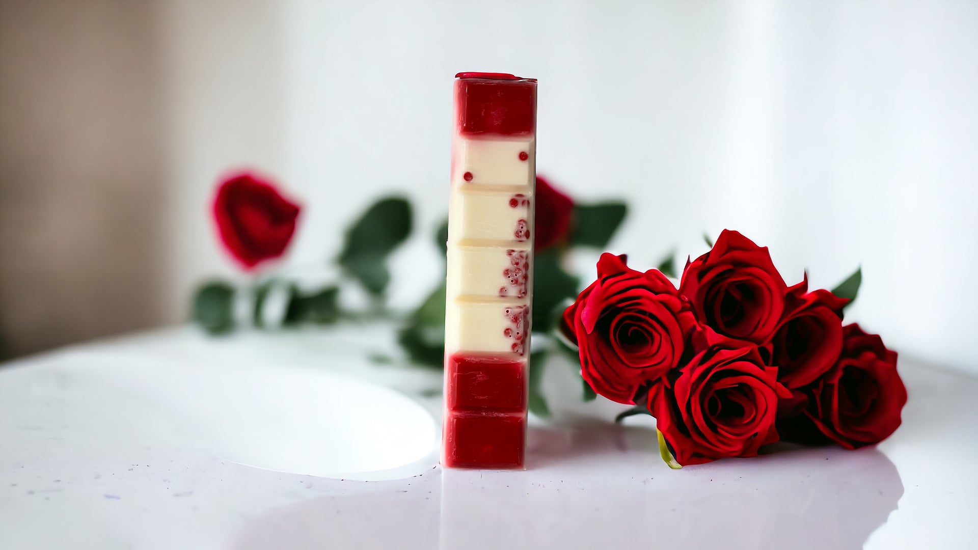 Red and white wax melt snap bar with red roses lying next to the wax melt on table.